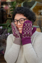 Load image into Gallery viewer, A person wearing a cream knit sweater and purple and beige patterned knit mittens, holding their hands up to their cheeks with glasses on, in an outdoor setting.