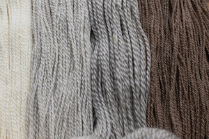 Close-up of gray yarn with a blurred brown and beige yarn in the background