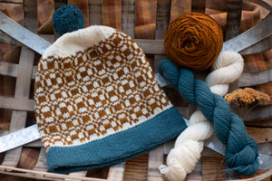 Knitted hat with a pattern on a wooden surface with yarn balls.