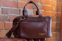 Load image into Gallery viewer, Brown leather bag with 'Re-Designed Project' logo against a brick wall.