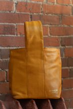 Load image into Gallery viewer, Yellow leather bag held against a brick wall