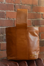 Load image into Gallery viewer, Brown leather bag with 'BC BAGUETTE' branding against a brick wall.