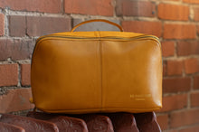 Load image into Gallery viewer, Brown leather toiletry bag with 'Redesigned' branding against a brick wall.