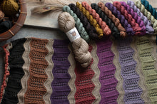 Load image into Gallery viewer, Colorful yarn skeins on a textured surface with a crocheted fabric sample.