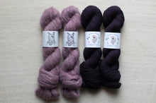 Load image into Gallery viewer, Two skeins of purple yarn and two skeins of black yarn on a beige background
