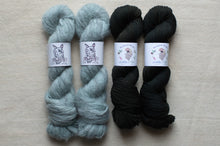 Load image into Gallery viewer, Two skeins of light blue yarn and two skeins of black yarn on a beige surface.