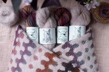 Load image into Gallery viewer, Four cylindrical containers with labels on a knitted fabric background