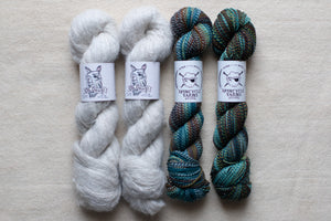 Two skeins of gray yarn and two skeins of multicolored yarn on a light gray background with 'Spincycle Yarns' labels.