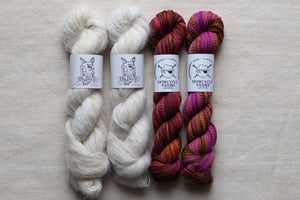 Two skeins of white yarn and two skeins of multicolored yarn on a neutral background with Spindles Yarns labels.