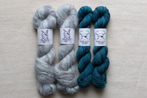 Two skeins of gray yarn and two skeins of blue yarn on a beige background with a brand label.