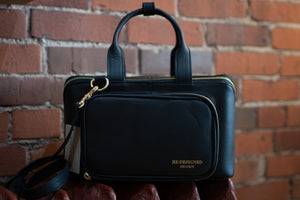 Black handbag with gold accents held against a brick wall