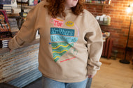 Person wearing a beige sweatshirt with colorful text and graphics in a store setting
