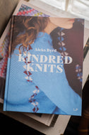 Book titled 'Kindred Knits' by Aleks Byrd on a stack of books.