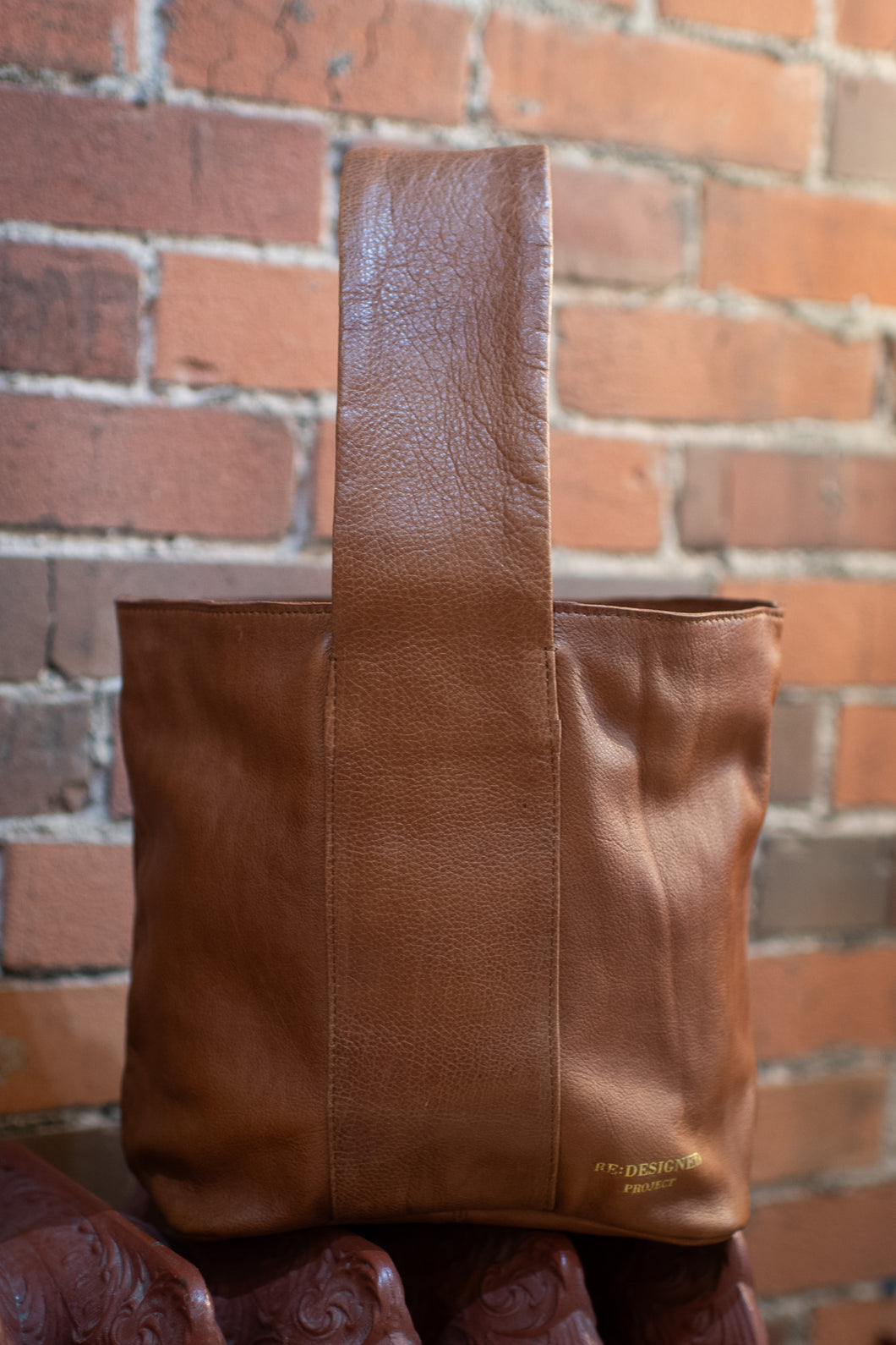Brown leather bag against a brick wall