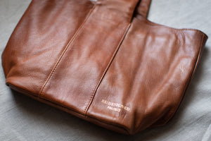 Brown leather bag with 'Redesigned Project' branding on a gray surface