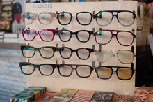 Load image into Gallery viewer, Display of various eyeglasses on a wooden stand with 'Caddis' branding.