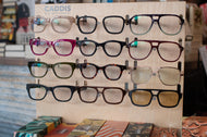Display of various eyeglasses on a wooden stand with 'Caddis' branding.