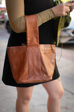 Load image into Gallery viewer, Brown leather tote bag held by a person on a street.