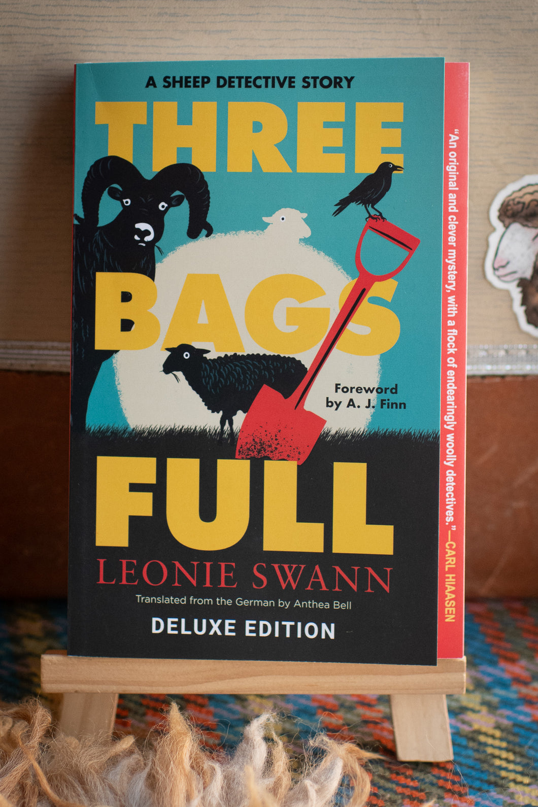 Book titled 'Three Bags Full' by Leonie Swann on a stand with a wooden background
