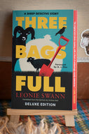Book titled 'Three Bags Full' by Leonie Swann on a stand with a wooden background