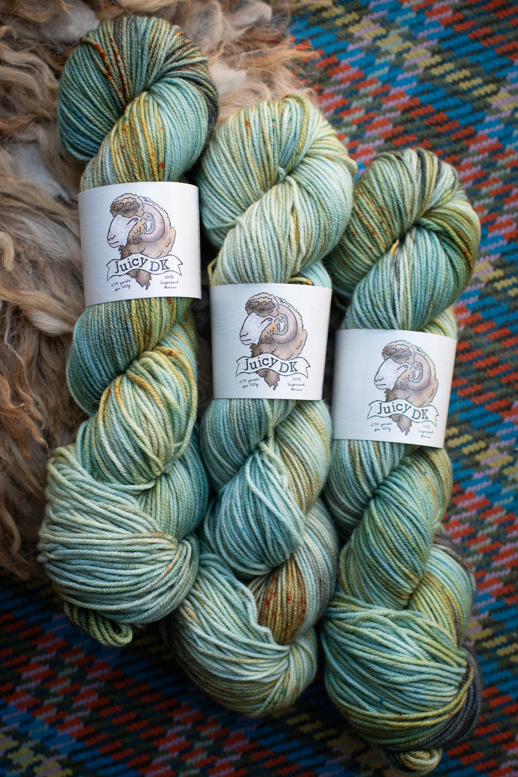 Three skeins of yarn with labels on a textured fabric background