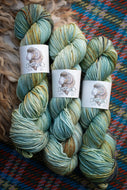 Three skeins of yarn with labels on a textured fabric background