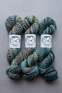 Three skeins of yarn with Plump Spincycle Yarns labels on a gray background