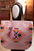 Load image into Gallery viewer, Pink tote bag with geometric pattern and tassel on a mannequin against a brick wall.