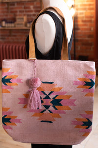 Pink tote bag with geometric pattern and tassel on a mannequin against a brick wall.