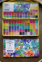 Load image into Gallery viewer, Open watercolor paint set with a watercolor pad on a wooden surface