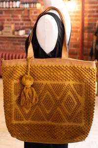 Brown knitted tote bag with a tassel on a mannequin against a brick wall background