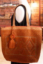 Load image into Gallery viewer, Brown woven handbag with a tassel on a mannequin against a brick wall background.