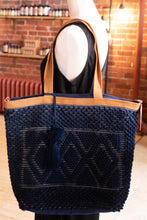 Load image into Gallery viewer, Navy blue woven tote bag with brown handles on a mannequin against a brick wall background.