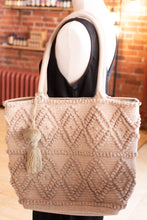 Load image into Gallery viewer, Beige textured tote bag with tassel on a mannequin against a brick wall background