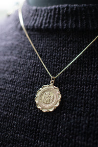 Gold necklace with a round pendant on a black textured sweater