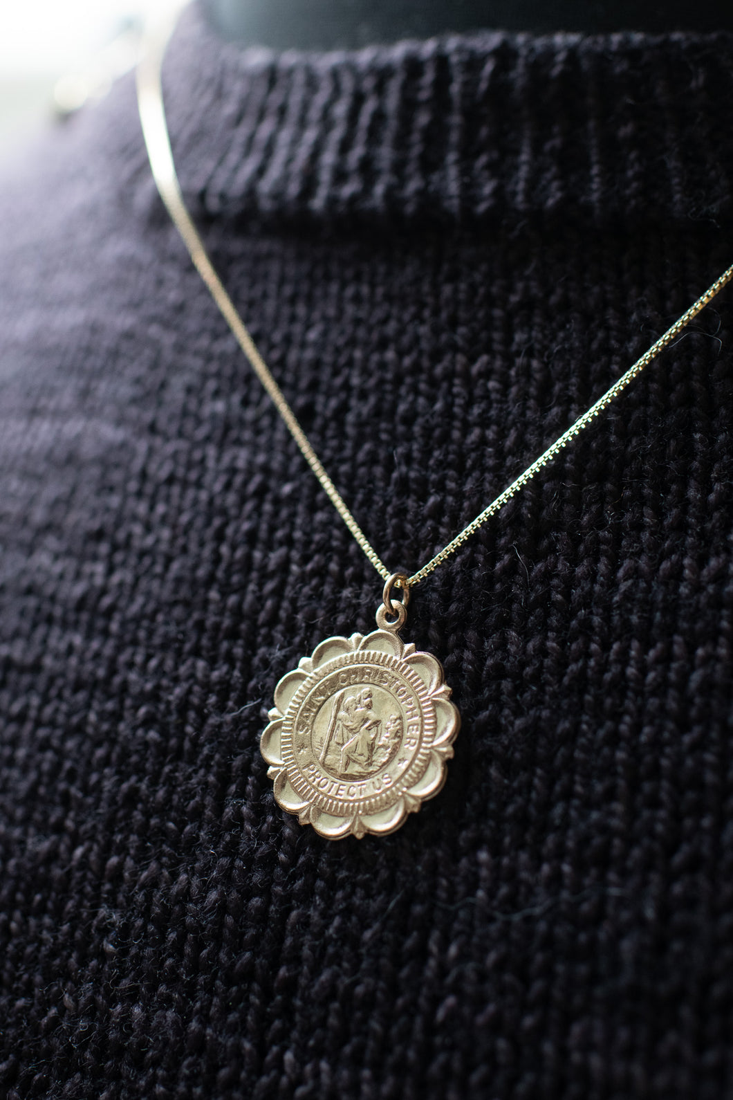 Gold necklace with a round pendant on a black textured sweater