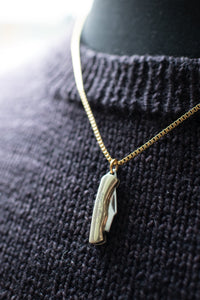 Gold necklace with a shoe-shaped pendant on a dark textured fabric background