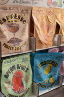 Assorted frozen cocktail packages on a shelf with branding and product names.