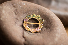 Load image into Gallery viewer, Gold brooch on a textured stone surface
