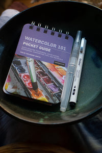 Watercolor pocket guide and markers on a dark surface
