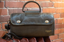 Load image into Gallery viewer, Brown leather satchel bag held against a brick wall