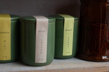 Load image into Gallery viewer, Three green candles with labels on a wooden surface next to a glass jar.