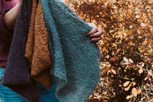 Load image into Gallery viewer, Person holding a stack of knitted sweaters with a natural background