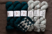 Load image into Gallery viewer, Three skeins of teal yarn and two skeins of white yarn on a brown surface with labels.