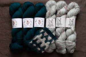 Three skeins of teal yarn and two skeins of white yarn on a brown surface with labels.