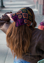 Load image into Gallery viewer, A woman viewed from behind wearing a brown leather jacket and a colorful crocheted granny-square beanie with long brown hair.