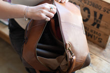 Load image into Gallery viewer, Brown leather bag with a person&#39;s hand opening it, wooden box in the background