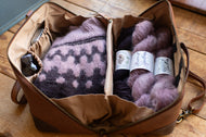 Open brown leather bag containing yarn and knitting supplies on a wooden surface