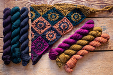 Load image into Gallery viewer, Five skeins of yarn in assorted colors arranged on a rustic wooden surface beside a crocheted swatch showing the yarn's texture and color combinations.