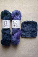 Load image into Gallery viewer, Two skeins of blue and purple yarn with labels and a knitted sample on a beige background